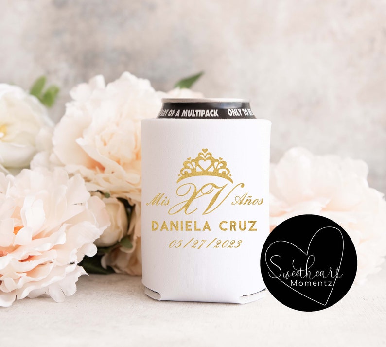 May include: White can cooler with a gold crown and the text "Mis XV A&ntilde;os Daniela Cruz 05/27/2023" and a black circle with the text "Sweetheart Momentz".