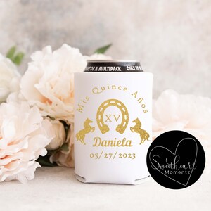 May include: White can cooler with gold text and graphics for a quincea&ntilde;era. The design includes a horseshoe, horses, the name "Daniela", and the date 05/27/2023. The words "Mis Quince A&ntilde;os" are also present.