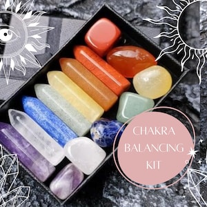 Puede incluir: Un conjunto de siete cristales de equilibrio de chakras en una caja negra. Los cristales están dispuestos en un orden de arcoíris, del rojo al violeta. La caja tiene una etiqueta que dice "Chakra Balancing Kit".