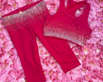 May include: A hot pink two-piece athletic set consisting of a racerback sports bra and cropped leggings. Both pieces feature a dense gradient of clear, reflective rhinestones concentrated at the waistband and the hem of the sports bra.