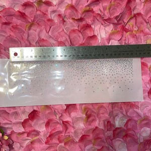 K&ouml;nnte beinhalten: Ein Bogen aus schillernden Strasssteinen auf einer transparenten Unterlage, gemessen mit einem Metalllineal. Die Strasssteine sind in einem Farbverlauf angeordnet. Das Lineal zeigt Messungen bis zu 33 cm.