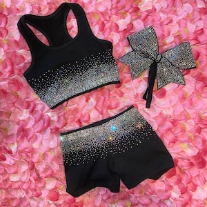 May include: A black athletic crop top and matching shorts set featuring a dense gradient of shimmering, multi-colored rhinestones across the upper sections. A large, coordinating black hair bow covered in sparkling rhinestones is included.