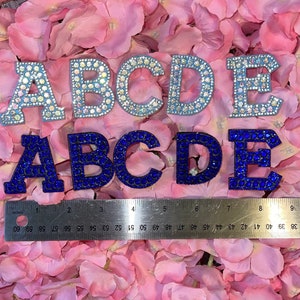 May include: Two sets of letters, A-E, made of rhinestones. The top set is light blue with clear rhinestones. The bottom set is dark blue with dark blue rhinestones.
