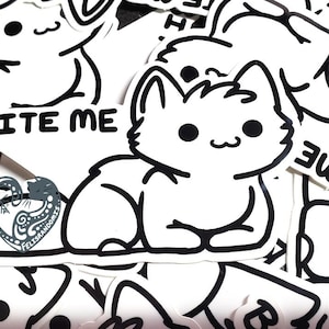 May include: A collection of white stickers with black outlines. The stickers feature a cartoon cat with the text "BITE ME". A heart-shaped sticker with a decorative design is also visible.