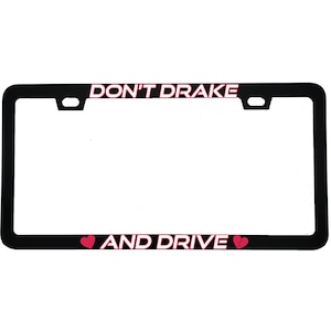 May include: Black license plate frame with the text "DON'T DRAKE" at the top and "AND DRIVE" at the bottom. The text is in a pink font. A pink heart graphic is on each side of the text "AND DRIVE".