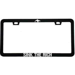 May include: Black license plate frame with the text "SINK THE RICH" in white block letters. A white orca whale graphic is in the upper right corner. The frame has a rectangular shape with rounded corners and mounting holes.