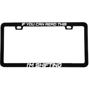 May include: Black license plate frame with white text that reads "IF YOU CAN READ THIS" at the top and "I'M SHIFTING" at the bottom. The frame has a rectangular shape with rounded corners.