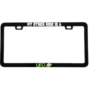 May include: Black license plate frame with the text "MY OTHER RIDE IS A" at the top and "UFO" with a cartoon UFO graphic at the bottom. The frame is rectangular with rounded corners.