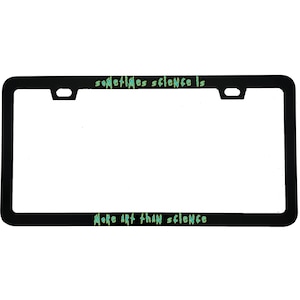 May include: Black license plate frame with the text "sometimes science is" at the top and "more art than science" at the bottom, in green lettering. The frame has a rectangular shape with rounded corners and mounting holes.