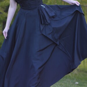 Pu&ograve; includere: Un abito maxi nero con un corpetto drappeggiato e una gonna fluida. La gonna ha un design a strati con un dettaglio a balze.