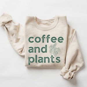 May include: A beige sweatshirt with the text "coffee and plants" in green lettering and a green leaf design.
