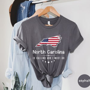 May include: A gray t-shirt with a graphic of the state of North Carolina with an American flag design. The text "North Carolina is calling and I must go" is printed below the graphic.