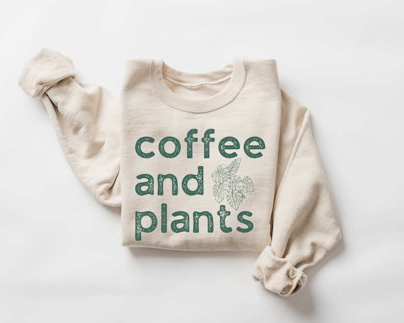 May include: A beige sweatshirt with the text "coffee and plants" in green lettering and a green leaf design.