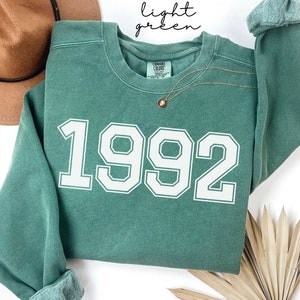 May include: A light green sweatshirt with the year 1992 printed in white on the front.