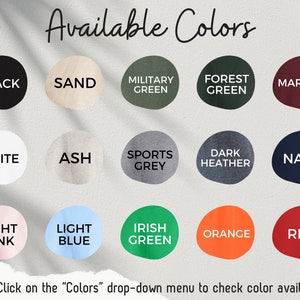 May include: A chart showing 18 different color options for a product. The colors include black, white, sand, ash, light pink, light blue, military green, forest green, sports grey, dark heather, navy, irish green, orange, and red. The text "Available Colors" is at the top of the chart.