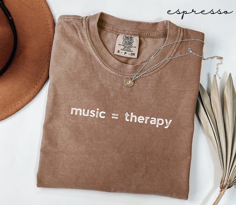 May include: A brown t-shirt with the text "music = therapy" embroidered in white. The shirt has a distressed look and is made of a soft, comfortable fabric.
