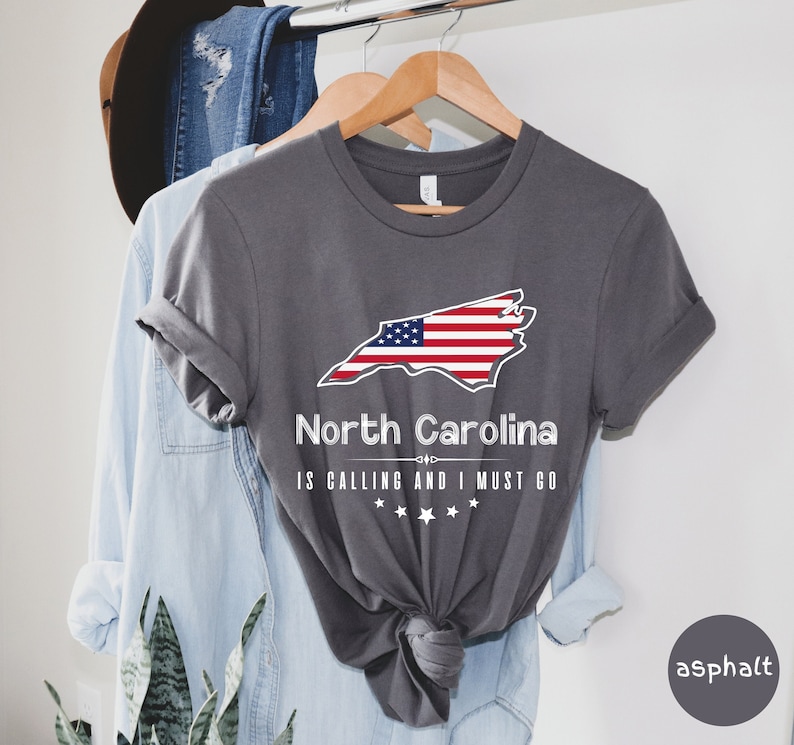 May include: A gray t-shirt with a graphic of the state of North Carolina with an American flag design. The text "North Carolina is calling and I must go" is printed below the graphic.