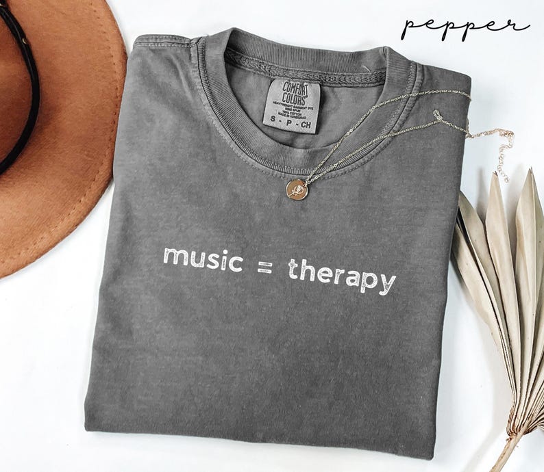 May include: Gray t-shirt with the text "music = therapy" embroidered in white. The shirt is made of a soft, comfortable fabric and has a relaxed fit.