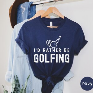 May include: Navy blue t-shirt with a white graphic of a golf club and ball. The text "I'd rather be golfing" is printed in white on the shirt.
