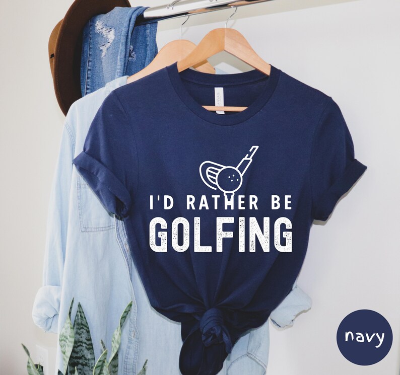May include: Navy blue t-shirt with a white graphic of a golf club and ball. The text "I'd rather be golfing" is printed in white on the shirt.