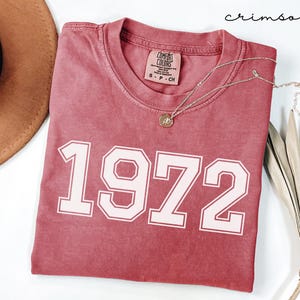 May include: A crimson red t-shirt with a white vintage-style 1972 graphic. The shirt is made of a soft, comfortable fabric and has a relaxed fit.