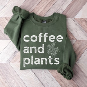May include: A green sweatshirt with the text "coffee and plants" in white lettering. The text has a distressed, vintage look.
