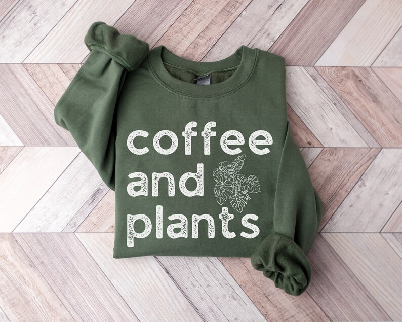 May include: A green sweatshirt with the text "coffee and plants" in white lettering. The text has a distressed, vintage look.