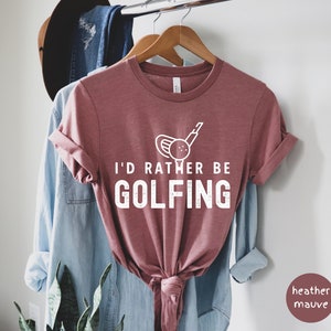 May include: A heather mauve t-shirt with a white graphic of a golf club and ball. The text "I'd rather be golfing" is printed in white on the shirt.