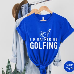 May include: A royal blue t-shirt with white text that reads "I'd rather be golfing" and a white graphic of a golf club and ball.