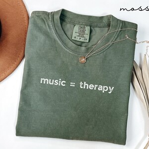 May include: A green t-shirt with the text "music = therapy" in white embroidery. The shirt is made by Comfort Colors and is a size S-P-CH.