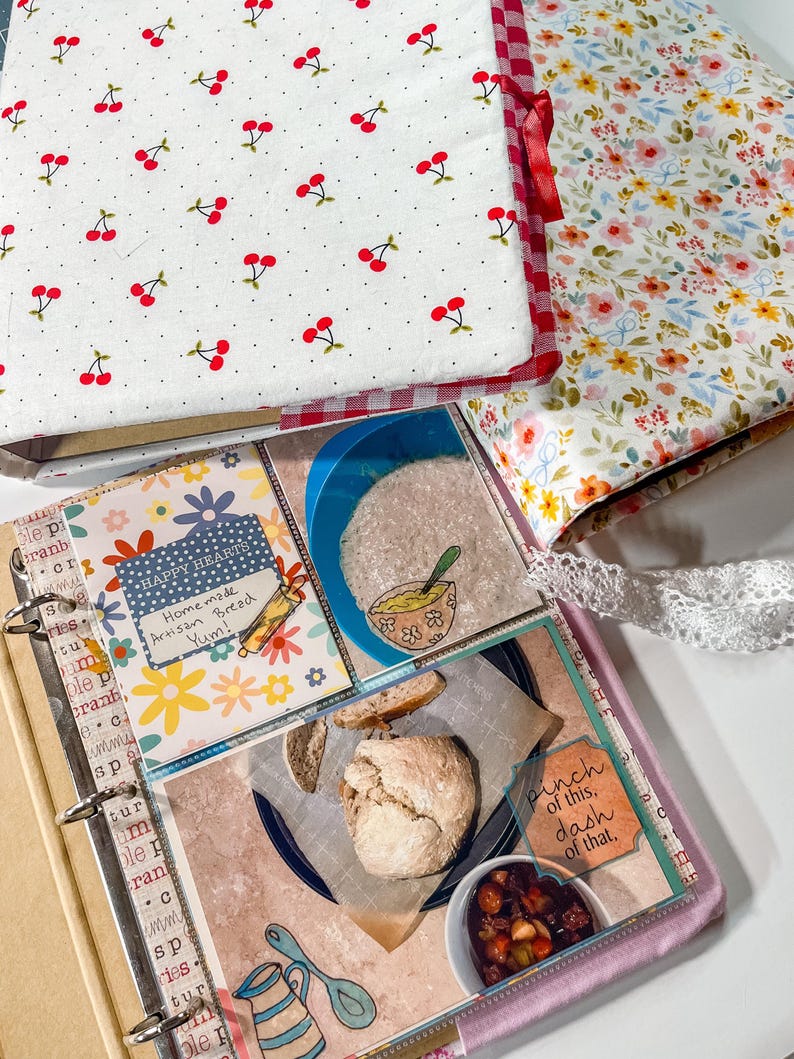 Puede incluir: Un archivador de recetas con una cubierta blanca con estampado de cerezas rojas y un lomo de cuadros rojos. Las p&aacute;ginas interiores muestran fotos de pan artesanal, un taz&oacute;n de sopa y el texto Happy Hearts Homemade Artisan Bread Yum! y pinch of this, dash of that.