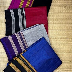 May include: A collection of folded fabric pieces in various colors, including black, red, blue, purple, and gray. Some pieces have decorative borders with gold and silver accents. The fabrics appear to be silk or a similar material, with a slight sheen.
