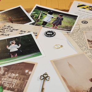 Peut inclure: Une collection de cartes postales et de photographies vintage, dont une photo en noir et blanc d'un bâtiment avec le texte "LIN ROUGE" dessus, une photo de deux jeunes filles en robe et une photo d'une balançoire dans un parc. Il y a aussi une clé dorée avec un motif de trèfle, une bague dorée et une puce noire avec le numéro "100" dessus.