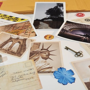 May include: A collection of vintage postcards featuring iconic landmarks like the Brooklyn Bridge, the Statue of Liberty, and the Eiffel Tower. The postcards are arranged on a white surface with a key, a compass, and a small blue flower.