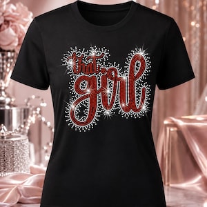 May include: A black short-sleeved t-shirt featuring the text "that girl" written in a cursive script. The lettering is filled with red rhinestones and outlined with white rhinestones, creating a sparkling effect across the chest area.