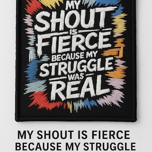 May include: Black embroidered patch with the text "MY SHOUT IS FIERCE BECAUSE MY STRUGGLE WAS REAL" in white. The patch has colorful embroidered accents in red, yellow, blue, and pink.