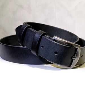 May include: A black leather belt with a silver buckle. The belt is rolled up, showing the buckle and the belt loop. The leather appears smooth and the buckle is rectangular.
