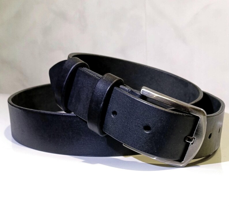 May include: A black leather belt with a silver buckle. The belt is rolled up, showing the buckle and the belt loop. The leather appears smooth and the buckle is rectangular.