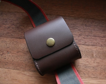 Può includere: Una pochette in pelle marrone con una chiusura a bottone in ottone attaccata a una cinghia a righe rosse e nere.