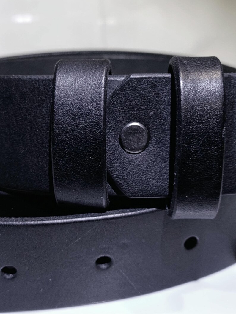 May include: Close-up of a black leather belt with a silver buckle. The belt has a classic design with a simple, elegant aesthetic. The leather appears smooth and durable, with visible stitching and a metal buckle.