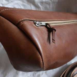 May include: A brown leather bag with a zipper closure and a strap. The bag has a rounded shape and a smooth texture.
