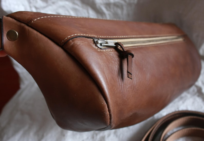 May include: A brown leather bag with a zipper closure and a strap. The bag has a rounded shape and a smooth texture.