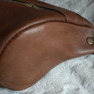 May include: A brown leather crossbody bag with a metal buckle and a zipper closure.