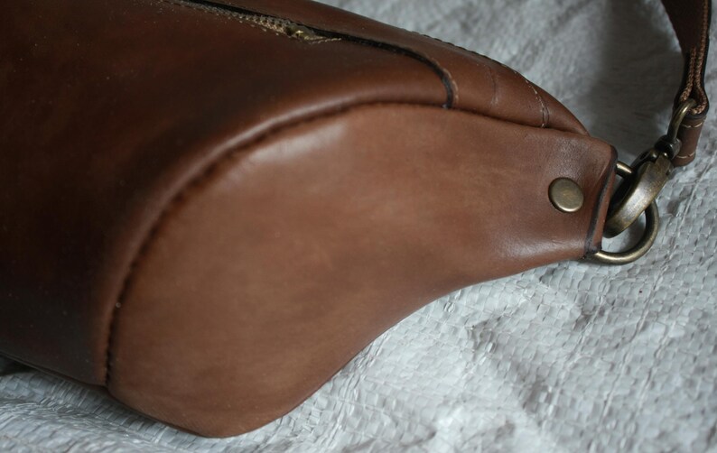 May include: A brown leather crossbody bag with a metal buckle and a zipper closure.