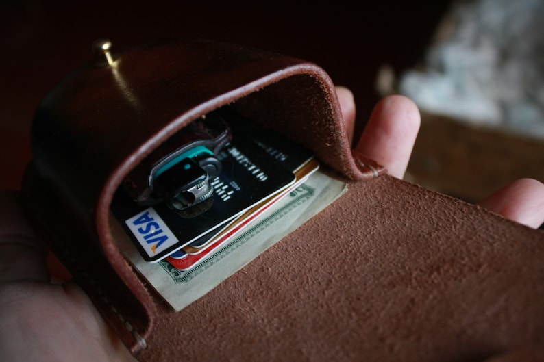 May include: A brown leather wallet with a flap that opens to reveal credit cards and cash. The wallet has a brass button closure.