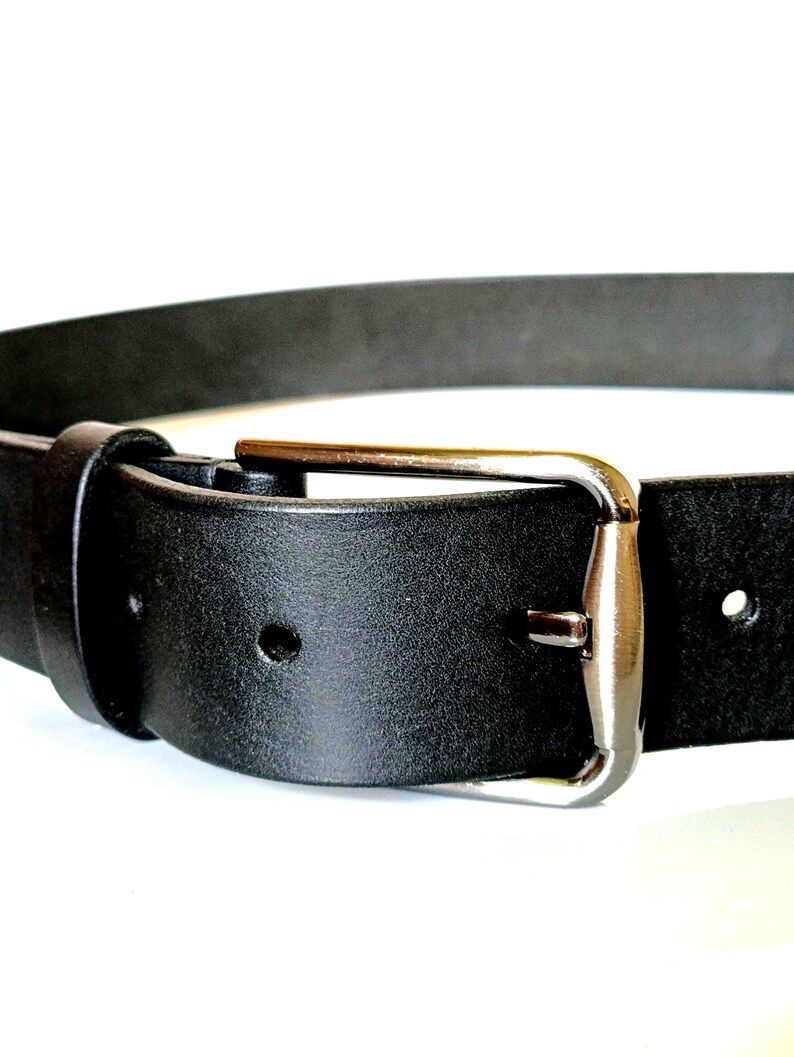 K&ouml;nnte beinhalten: Nahaufnahme eines schwarzen Lederg&uuml;rtels mit silberner Schnalle. Der G&uuml;rtel hat ein klassisches Design mit rechteckiger Schnalle und einer Schlaufe. Das Leder wirkt glatt. Der G&uuml;rtel ist etwa 3,2 cm breit.