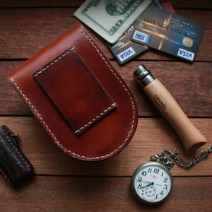 May include: A brown leather pouch with a white stitch detail, a pocket knife with a wooden handle, a pocket watch with a silver chain, and a lighter with a black and blue patterned design.