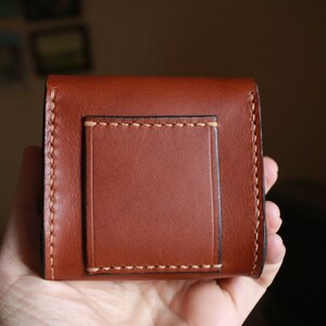 May include: A brown leather wallet with a stitched flap and a smaller pocket on the front.