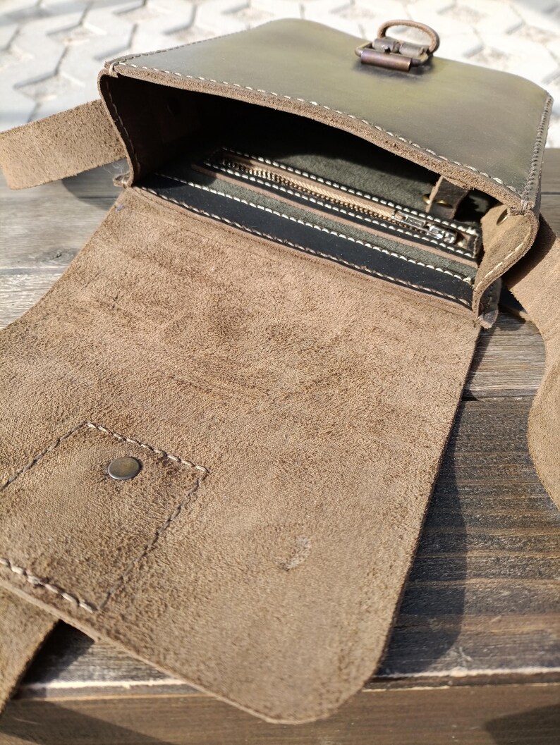 Pu&ograve; includere: Una borsa a tracolla in pelle marrone con una tasca con cerniera e una chiusura a lembo. La borsa ha una tracolla in pelle marrone e una fibbia in metallo.