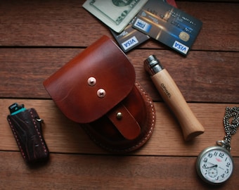 May include: A brown leather pouch with a snap closure, a pocket knife with a wooden handle, a pocket watch with a silver chain, and a lighter with a brown leather case.
